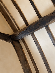 Close-up of the exposed dark-stained timber beams and smooth lime-washed infill panels where the framing meets the ceiling