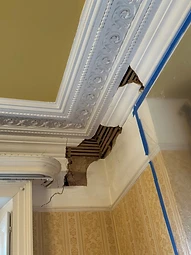Damaged plaster cornice broken away to expose timber laths, marked with investigative tape
