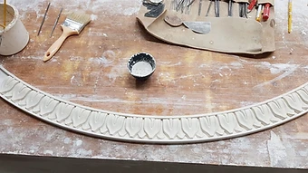 A curved run of decorative plaster moulding laid out among casting tools on the bench