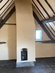 The vaulted bedroom with a lime-plastered chimney breast and fireplace beneath exposed rafters