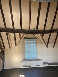 A finished room with louvered window shutters set within a timber-framed lime-plastered wall