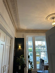 The finished room with a pendant-lit ceiling rose and restored cornices above a dark accent wall
