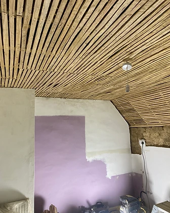 A wall stripped back to exposed timber laths beside a plastered finish built up in successive coats