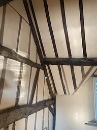 The completed vaulted bedroom, with exposed dark-stained timber framing and smooth lime-plastered infill panels beneath the angled roof