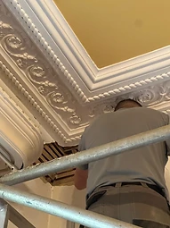 A craftsman working on an ornate plaster cornice from scaffolding