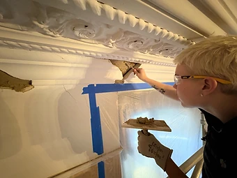 A craftsman precision-applying wet plaster to a damaged section of ornate cornice