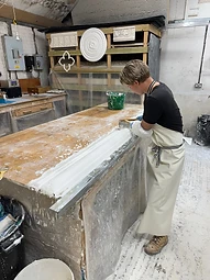 A young apprentice smoothing a line of fresh plaster on the workshop bench