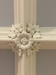 A central plaster boss of a Tudor rose flanked by foliage at the intersection of two mouldings