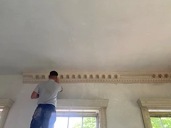 A craftsman fitting and finishing a run of newly installed decorative plaster cornice where it meets the ceiling