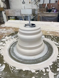 A bell-shaped fibrous plaster component mounted on a rotating casting table with a threaded steel reinforcement rod