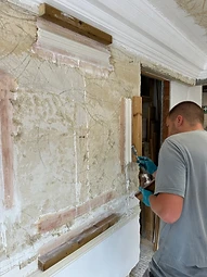 A plasterer applying plaster to a prepared wall set out with guide battens for decorative mouldings