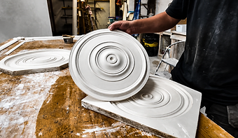 A craftsman handling freshly cast plaster ceiling medallions on the bench