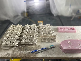 Cast plaster leaf enrichments and pink silicone moulds arranged on a dust-covered workbench