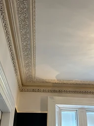 A corner view of the completed ornate cornice above a dark-painted wall