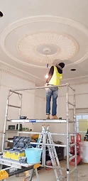 A plasterer in a hi-vis vest working from scaffolding on the large circular ceiling rose