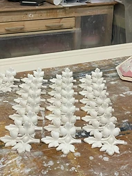 A grid of freshly cast plaster trefoil and fleur-de-lis motifs arranged on a weathered workshop bench