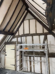 The gable end of the vaulted bedroom during the works, with exposed timber truss, lime-plastered panels and a traditional plank door beside scaffolding