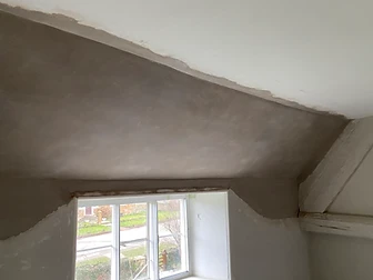 Finished lime plaster to a wall beneath a casement window, meeting the existing painted plaster, with a weathered timber beam at the left