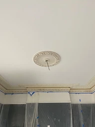 The restored ceiling rose and ornate cornice in place, with protective sheeting below indicating ongoing works