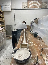 A craftsman smoothing a run of bespoke plaster moulding on the bench