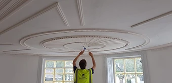 A craftsman in a Classic Plasterwork vest fixing the central point of the ceiling rose from below