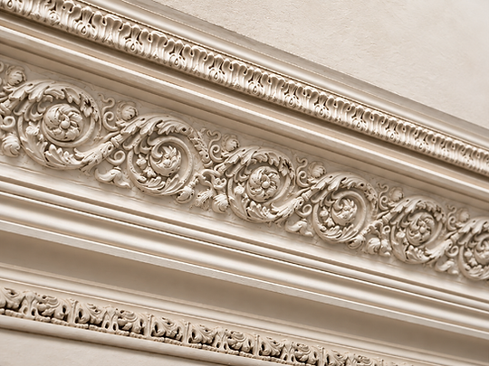 An angled, low-angle view of ornate Victorian plaster cornice work with floral and scroll-work motifs