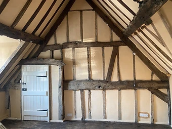 The timber-framed truss of the vaulted bedroom with exposed dark-stained timbers and warm lime-plastered infill panels beneath the pitched roof