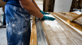 A craftsman's gloved hands pressing hessian scrim into wet plaster on the workshop bench