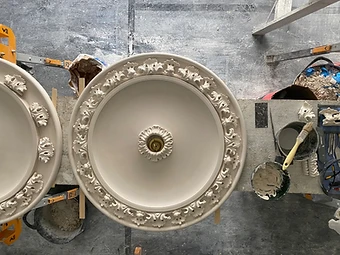 Top-down view of two large finished ceiling roses on the workbench, surrounded by plaster mix and casting tools