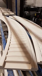 Two curved fluted fibrous plaster moulding sections resting on blue workshop racking