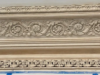 Close-up of the restored cornice showing crisp acanthus scrollwork and leaf borders with sharp, deep shadows