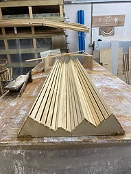 A wooden bench former shaped to the cornice profile, set up on the workbench
