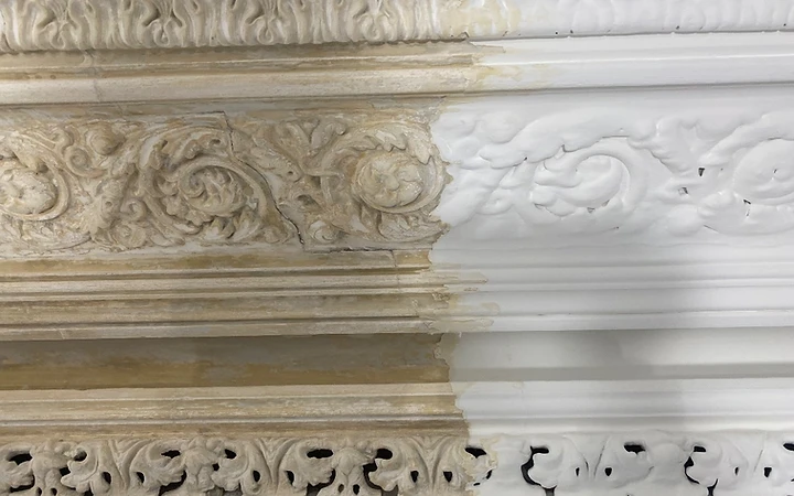 Close-up of a cornice split vertically between old discoloured paint on the left and freshly cleaned white plaster on the right