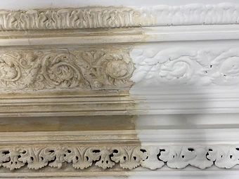 Close-up of a cornice split vertically between old discoloured paint on the left and freshly cleaned white plaster on the right