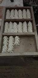 A wooden casting tray filled with rows of freshly cast white plaster leaf enrichments