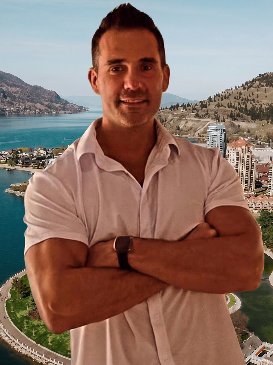 Corey Severin with arms crossed in a white short-sleeved shirt, edited in front of an aerial view of downtown Kelowna and the lake