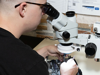 Aiden performing precision motherboard repair under a stereo microscope