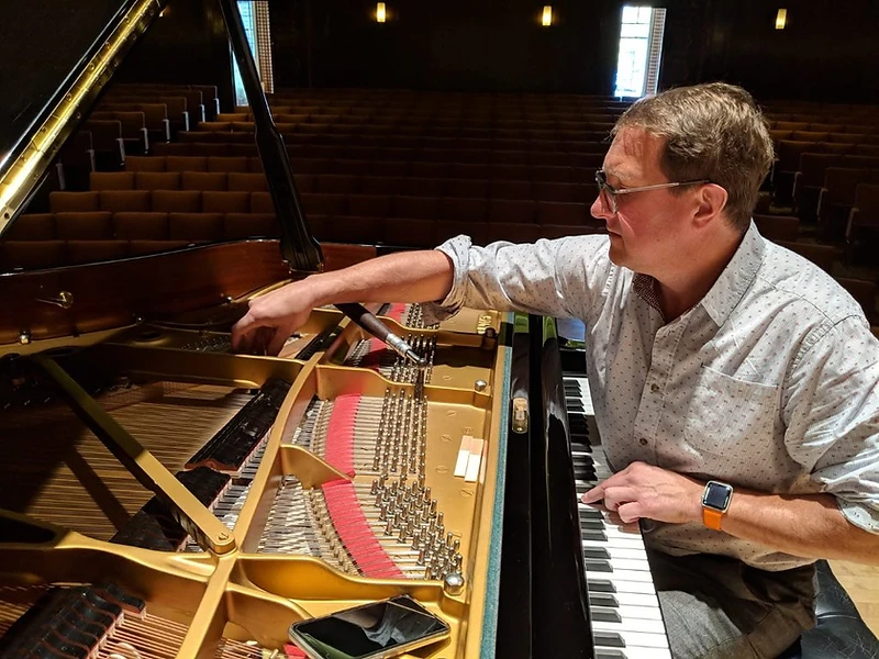 John Chapman tuning a grand piano in a concert hall