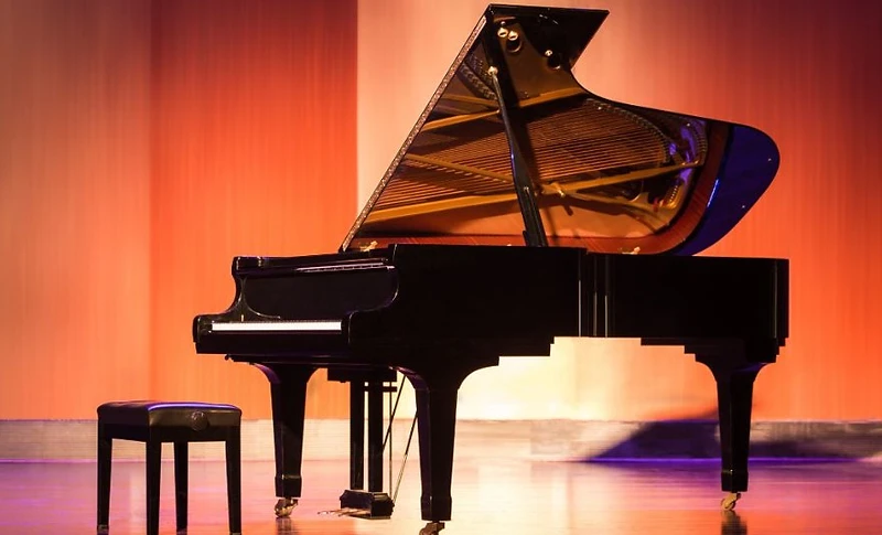 A grand piano on a concert hall stage under warm lighting