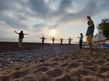 Group practicing Qigong on a pebble beach at golden hour