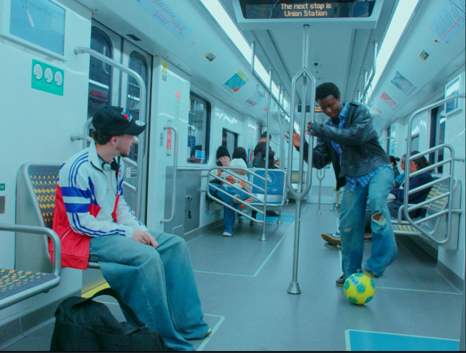 Interior de vagón de metro con tonos cian donde dos jóvenes juegan con un balón