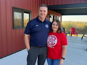 A guest in a Patriot Ranch polo and a volunteer in a Patriot Ranch tee outside the red barn
