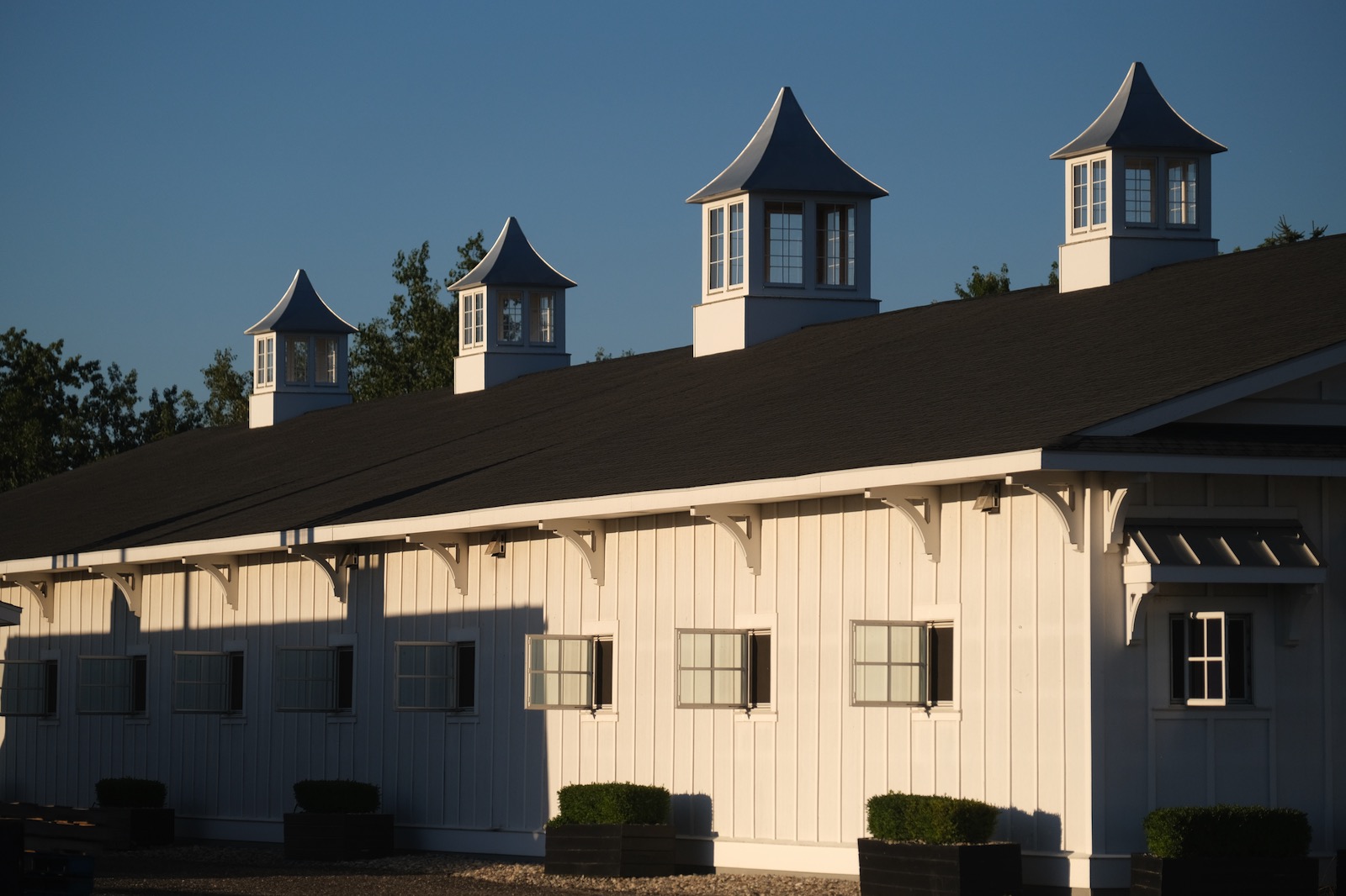 Three white cupolas with grey pyramidal roofs along a white board-and-batten building roofline against a clear blue sky