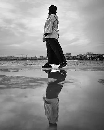 A person walking along a wet surface by the water