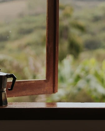 A moka pot and mug on a wooden windowsill overlooking green hills