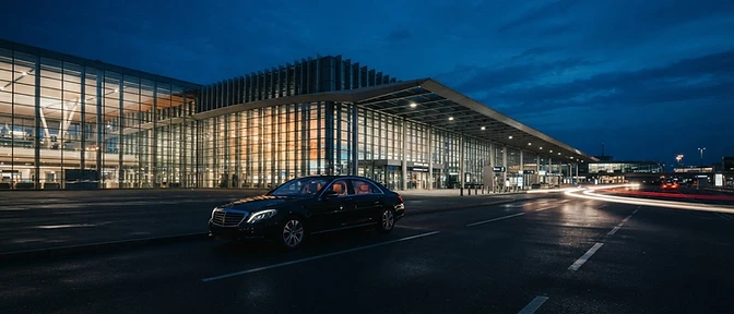 Executive sedan at glass-fronted airport terminal at dusk