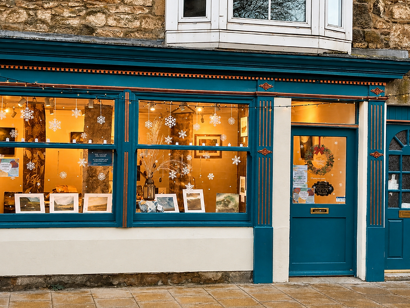 Cheviot House storefront on Wooler High Street, decorated for the holidays with snowflakes and warm gallery light