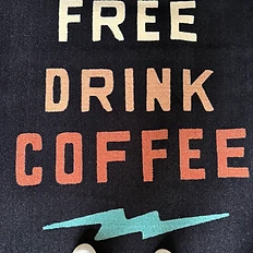 Top-down view of a dark floor mat reading Stay Free Drink Coffee with a teal lightning bolt