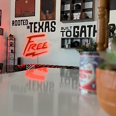 Tradition candle and succulent on a marble counter with the Rooted in Texas Built to Gather wall and FREE neon sign beyond