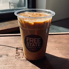 Iced coffee in a branded Free State cup topped with cinnamon, resting on a laser-etched wooden tray